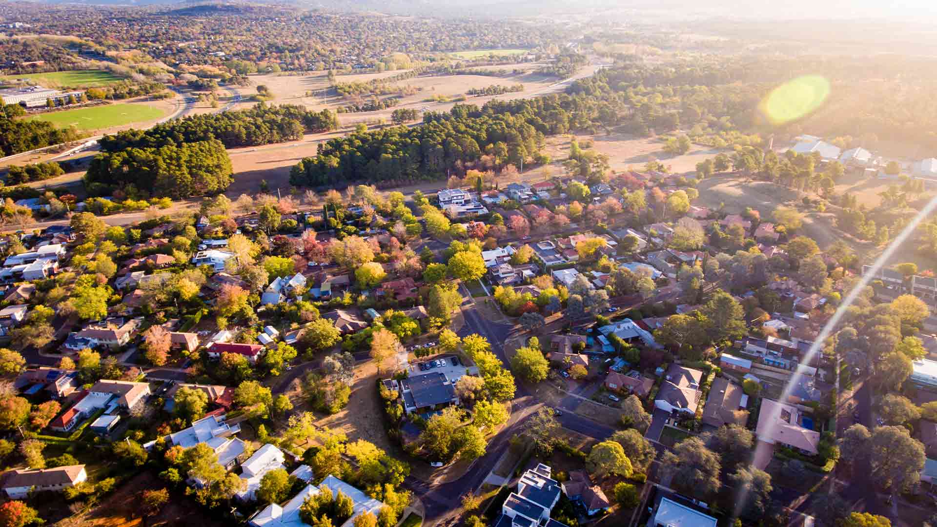Aerial photograph of suburban single-family homes in a tree-filled neighborhood at sunrise