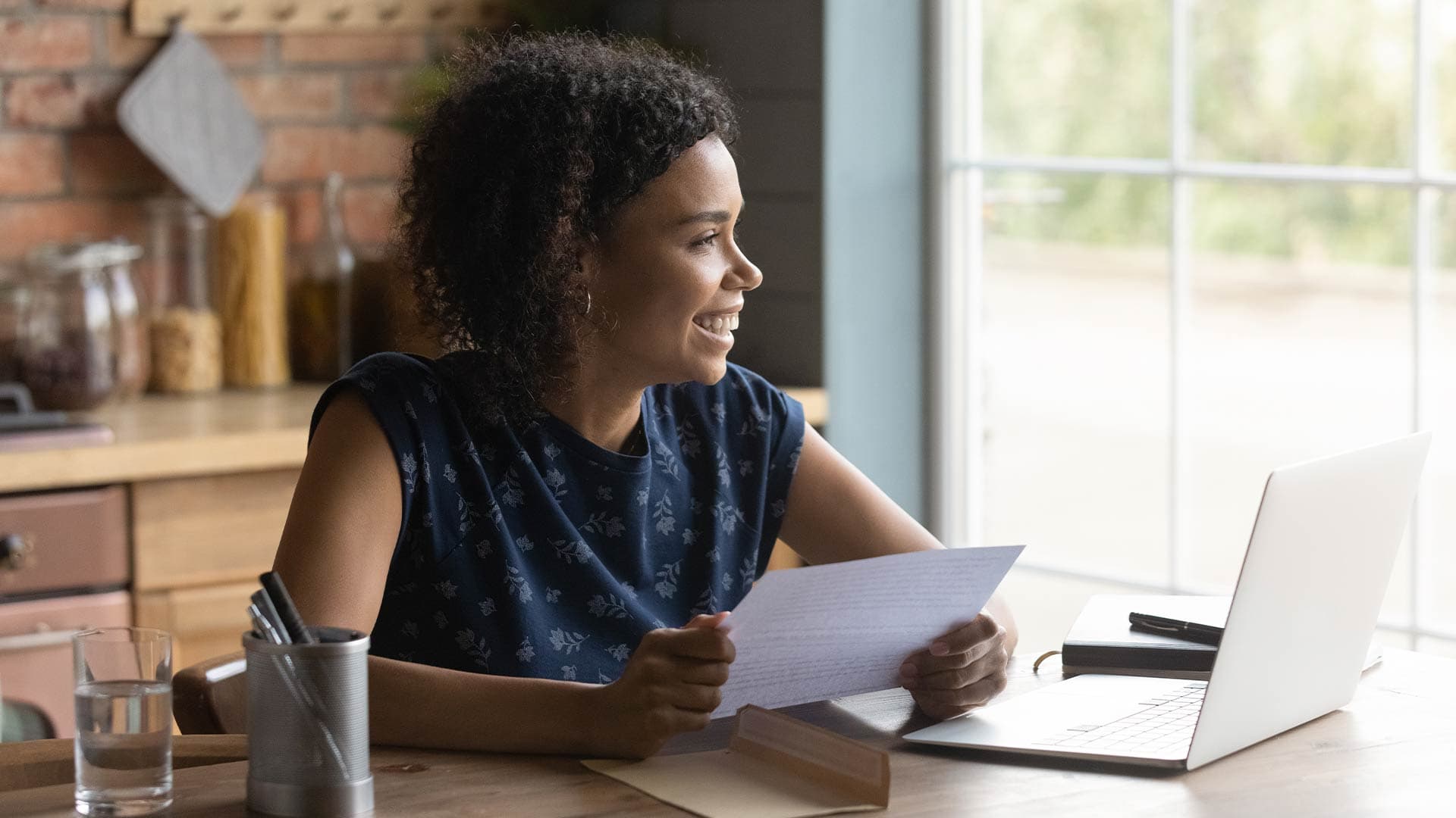 Young woman in her kitchen holding an offer letter for a new job