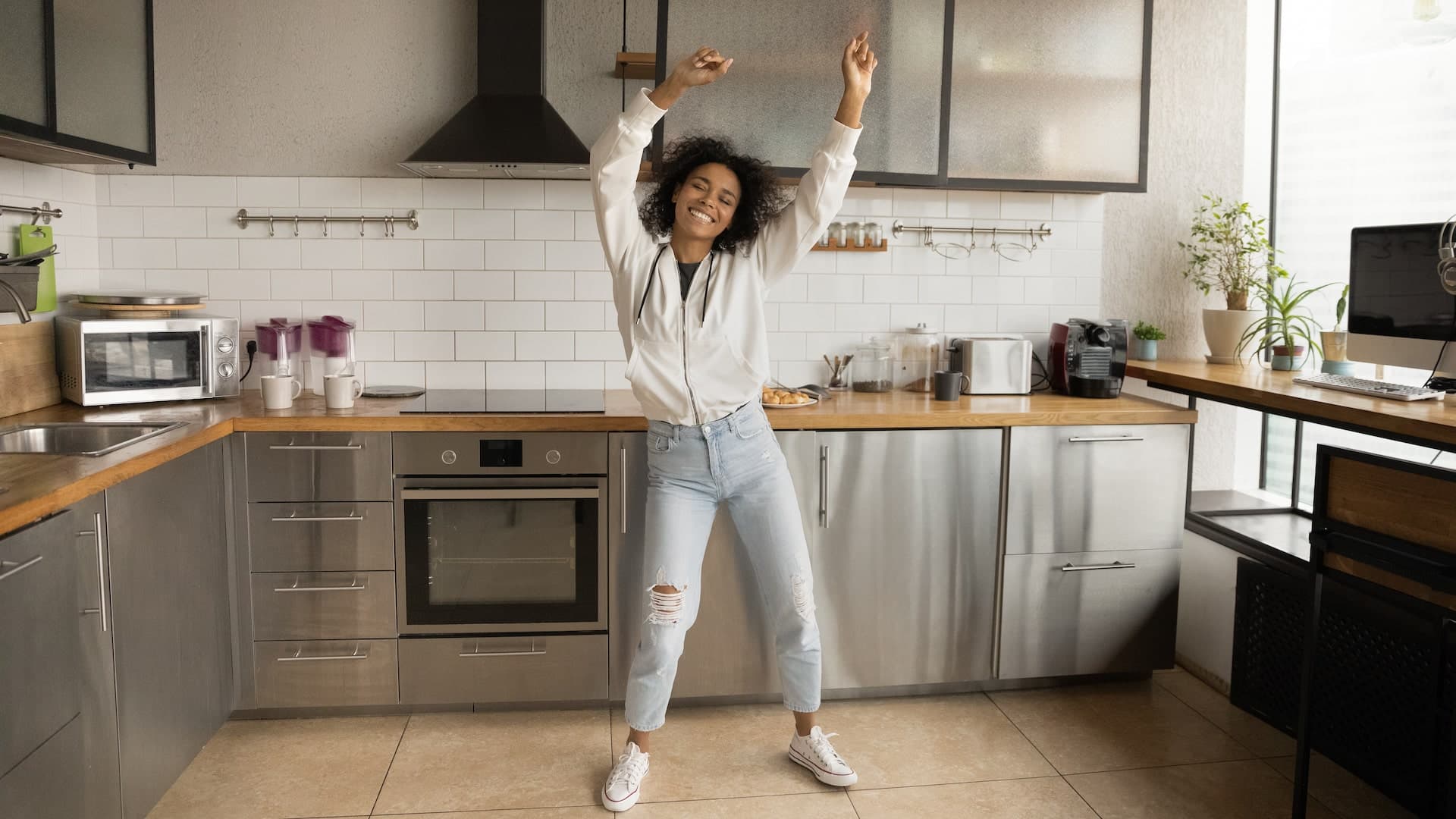 A woman in her 30s celebrates by dancing in the kitchen.