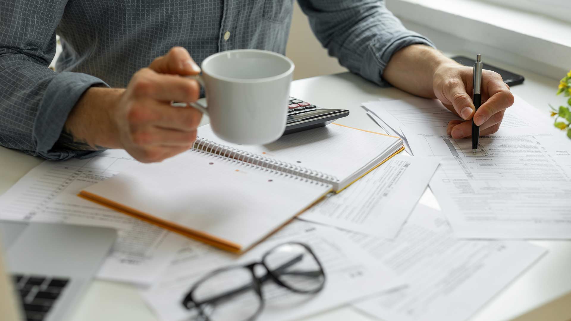 Young man looking at financial papers with a cup of coffee in his hand.