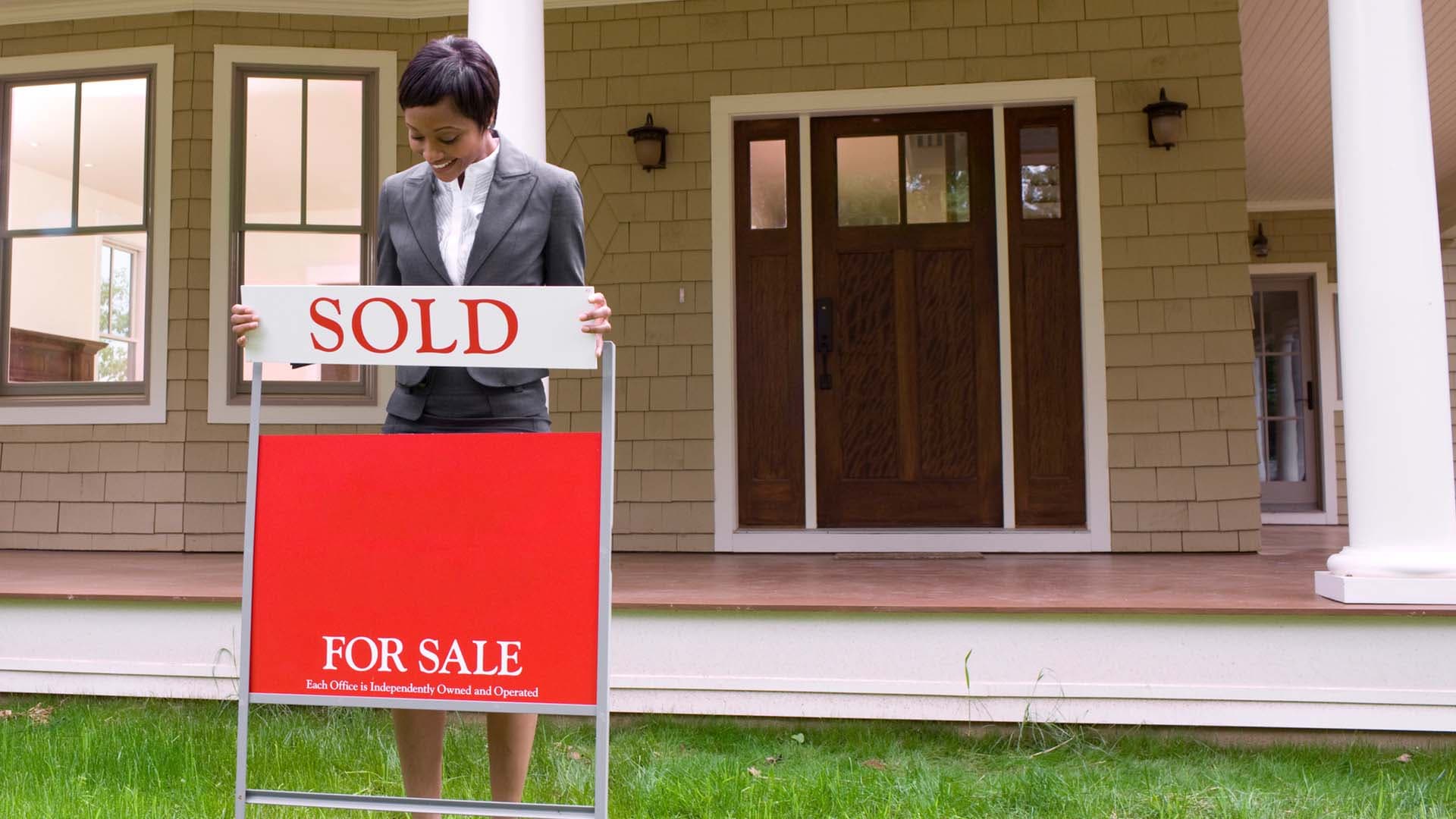A real estate agent puts a 'sold' sign in front of a listed house